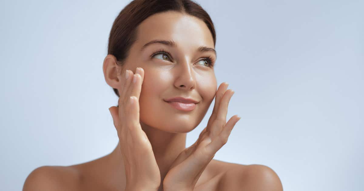 A woman gently touches her flawless and radiant face.